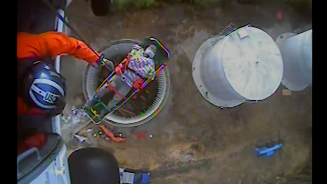 A construction worker is hoisted into the Coast Guard helicopter.